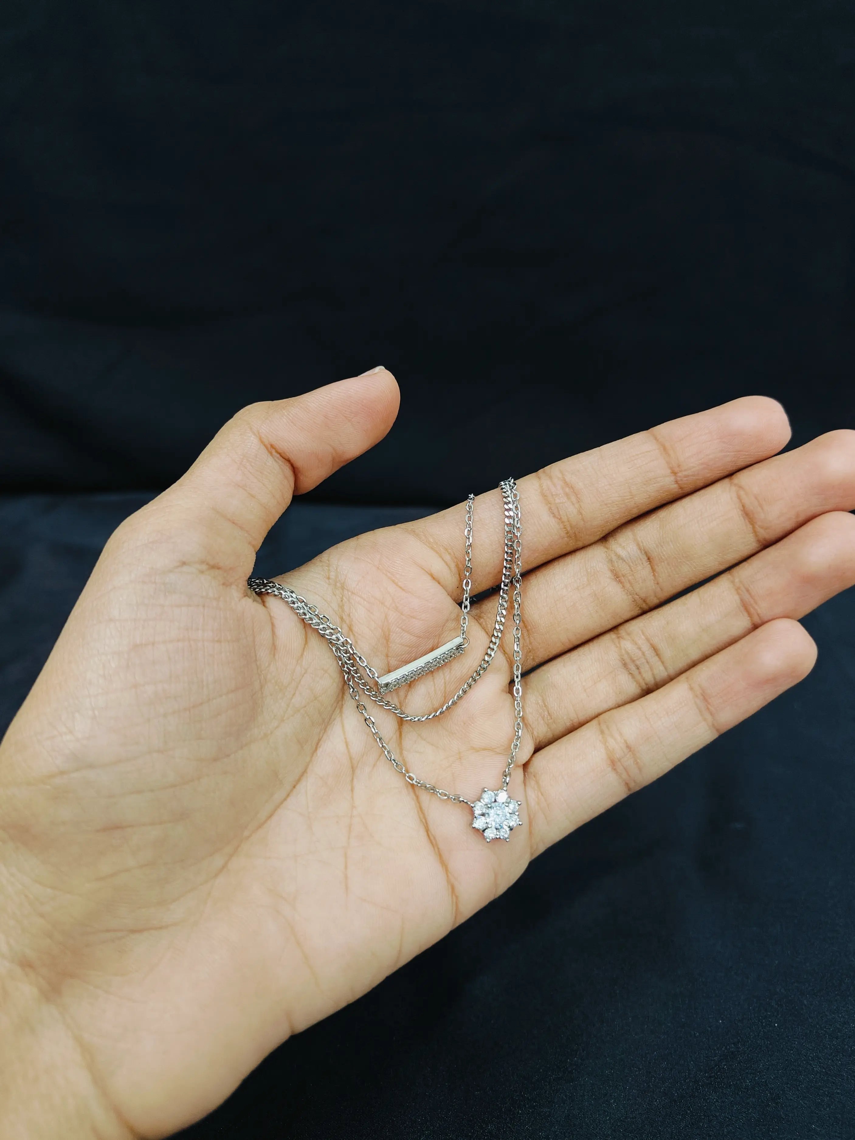 Hand holding two silver necklaces against a black background